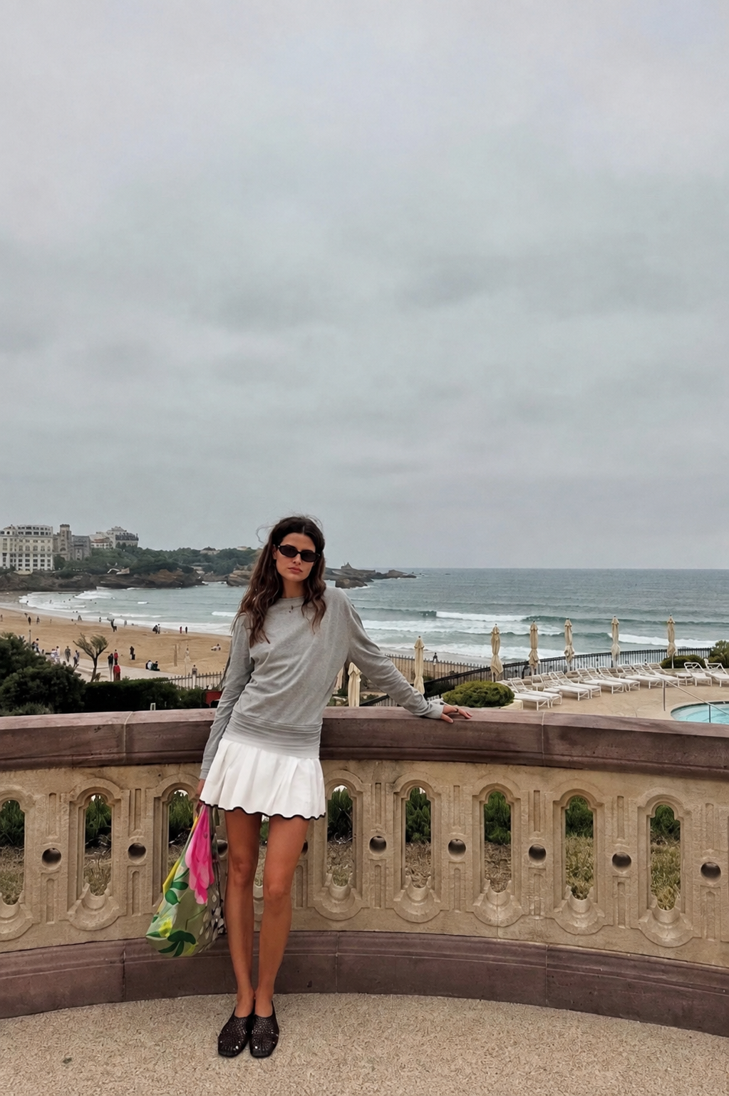 Model in a grey top and white skirt overlooking a beach